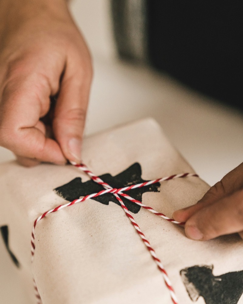Fingers drawing baker twine tight over a kraft wrapped parcel, the paper creased sharp