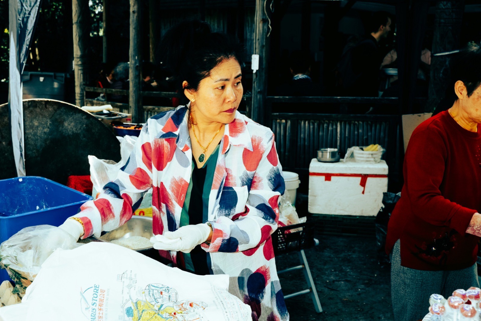 A wrapper working a covered market counter at night, stock and paper stacked around her