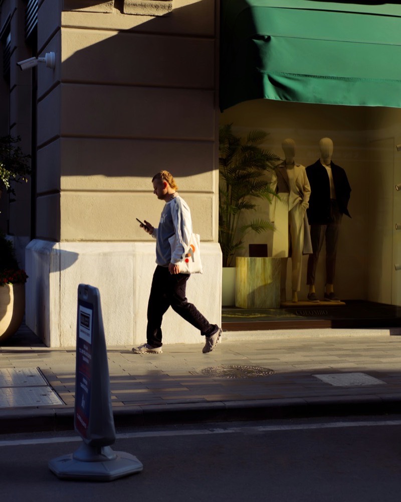 A customer books a slot on a phone while walking past lit shop windows
