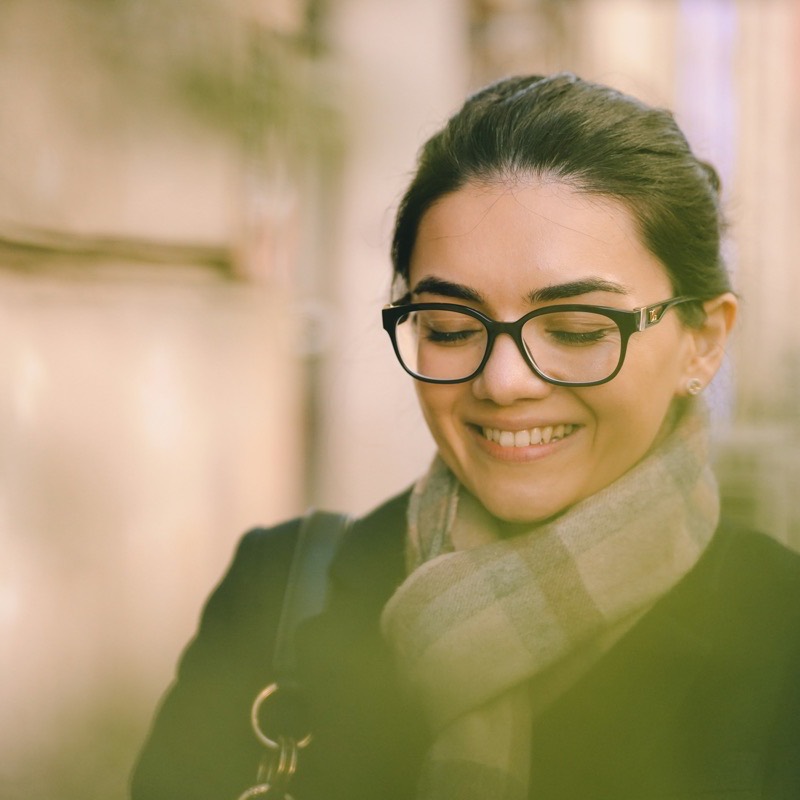 A customer in glasses and a wool scarf, warm street light across her shoulder