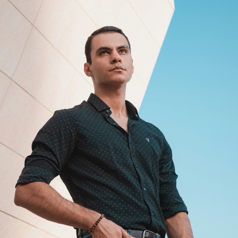 A customer stands against a pale wall with sleeves rolled, bright sky behind him